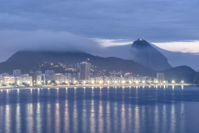 Illuminated city by sea against sky at night