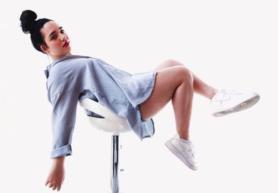 Young woman looking away while sitting against white background