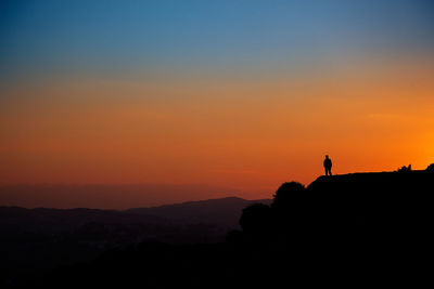 Silhouette man standing on cliff against sky during sunset