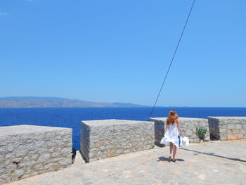 Full length of woman in white dress walking at observation point by sea against clear sky