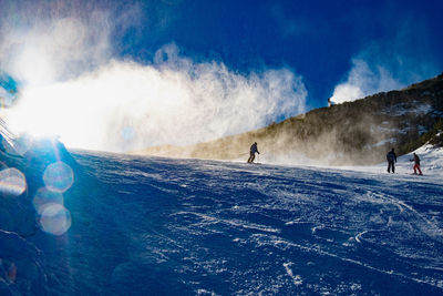 People downhill skiing below working snow canon. ski slopes on a sunny day, snow canon in action.