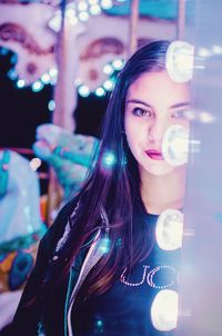 Portrait of beautiful young woman against illuminated lights