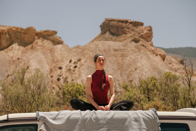 Low angle view of woman meditating while sitting on car roof