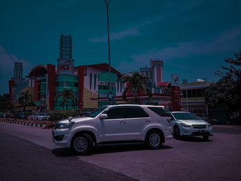 Cars on road by buildings in city against sky