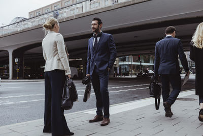 Entrepreneur with bag talking to female coworker while standing in city