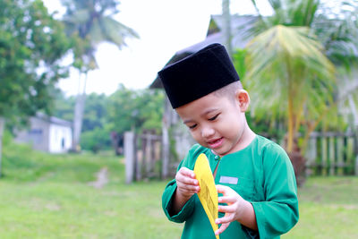 Smiling boy in traditional clothing holding envelope while standing on field