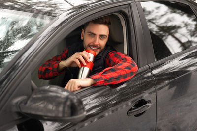 Portrait of a smiling young man sitting on car