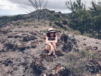 Portrait of young woman sitting on landscape against sky