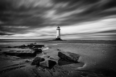 Lighthouse on rocks by sea against sky