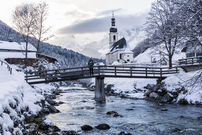 Person standing on bridge over river amidst houses during winter