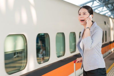 Young woman talking on phone by train at railroad station