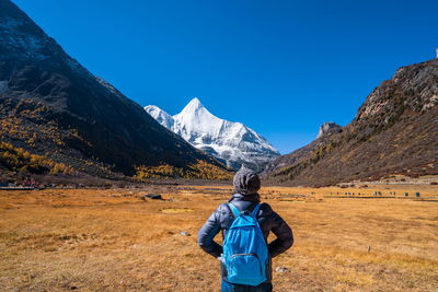 Rear view of man on snowcapped mountain against blue sky