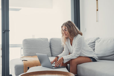 Young woman using laptop while sitting on sofa at home