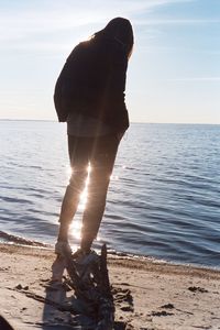 Rear view of man standing at sea shore against sky