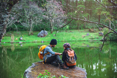 People sitting by lake against trees in forest