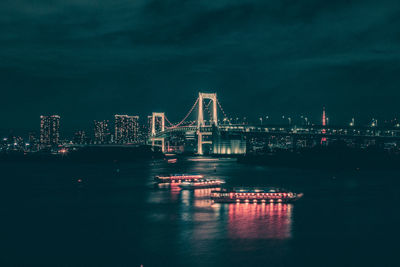 Illuminated bridge over river in city against sky at night