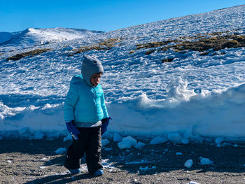 Child walking through the snow in the mountains with a blue coat looking at the ground