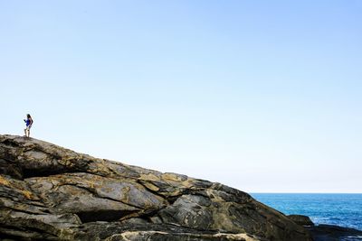 Woman standing on rock by sea against clear blue sky