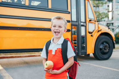 Smiling boy looking away while standing against bus