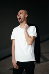Laughter one handsome young white man with a bald head in a white t-shirt on a dark urban background