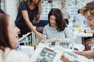 Midsection of owner showing menu to woman sitting in restaurant with friends