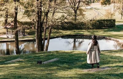Young woman in autumn clothes, coat, walking by pond in park.