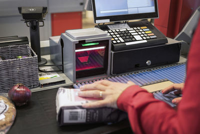 Cropped hand of female cashier at supermarket checkout counter