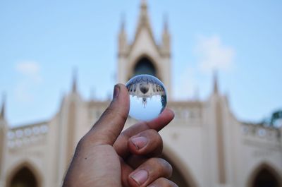 Cropped hand holding crystal ball with reflection against historic building