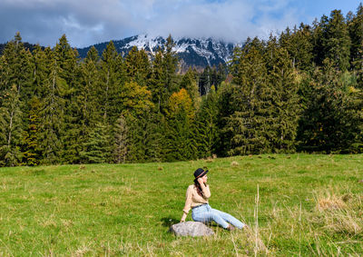 Young woman sitting in the middle of a green pasture in mountains.