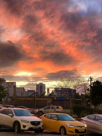 Cars on road by buildings against sky during sunset
