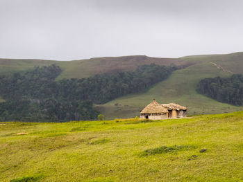 House on field by mountain against sky