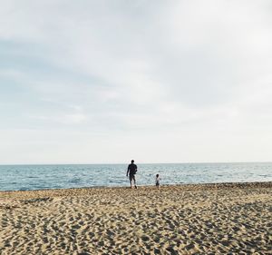 Father and son standing on sand against sea at beach