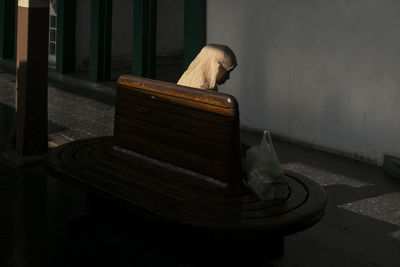 Side view of mid adult woman wearing hijab sitting on bench against wall