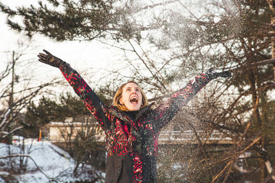 Smiling young woman throwing snow mid air during winter