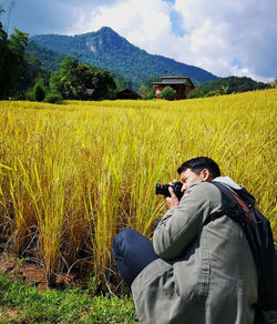 Man photographing while crouching on field against sky
