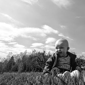 Cute baby boy sitting on grass against sky