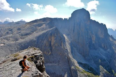 Backpacker looking at mountains while kneeling on cliff