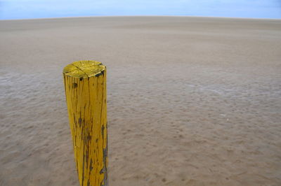 Yellow wooden post on sand at beach against sky