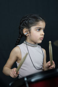 Girl wearing hearing aid while playing drum against wall