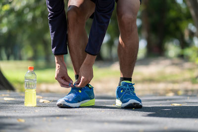 Low section of man tying shoelace by bottle on road