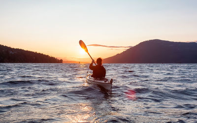 Rear view of man on sea against sky during sunset