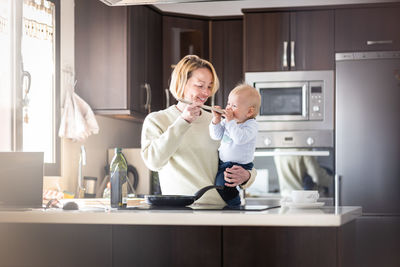 Happy mother and little infant baby boy cooking and tasting healthy dinner in domestic kitchen