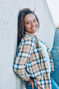 Portrait of smiling young woman standing by wall