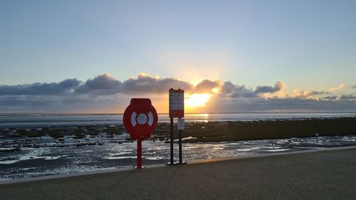 Road sign on beach against sky during sunset