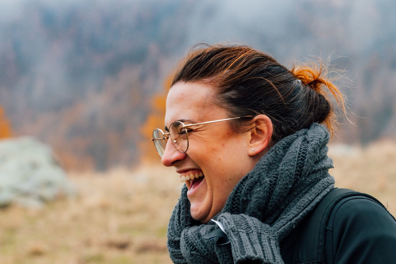 one person, headshot, real people, focus on foreground, leisure activity, lifestyles, glasses, portrait, looking away, side view, happiness, young adult, looking, smiling, eyeglasses, winter, young women, women, nature, warm clothing, scarf, outdoors, mouth open, hairstyle, profile view