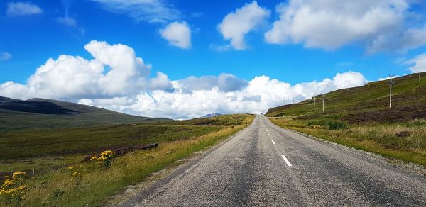 Empty road amidst landscape against sky