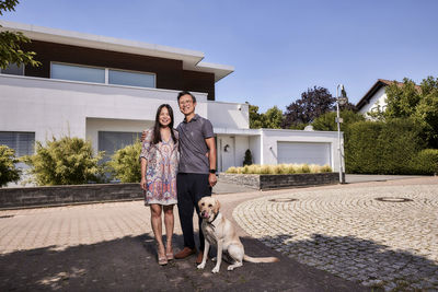 Happy couple with pet dog standing in front of house