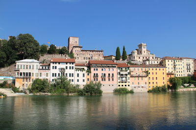 Buildings by river against clear blue sky