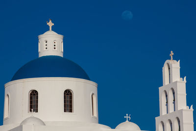 Dome and bell tower of the church of panagia platsani and the moon in oia city at santorini island