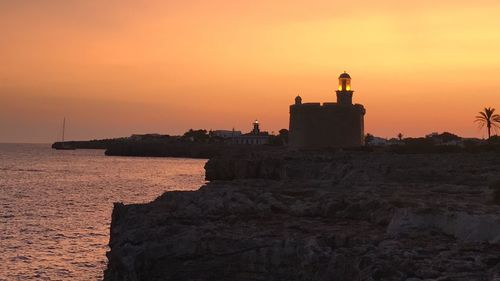 Lighthouse by sea against orange sky